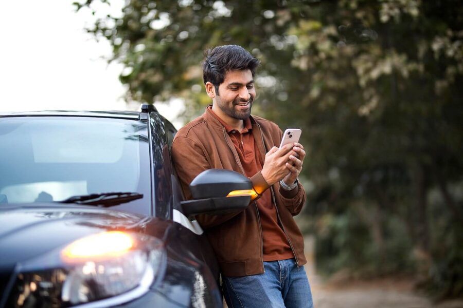 Smiling man checking his smartphone while leaning against his car