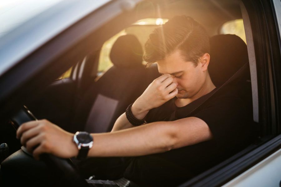 man holding one hand on face in distress while driving a car