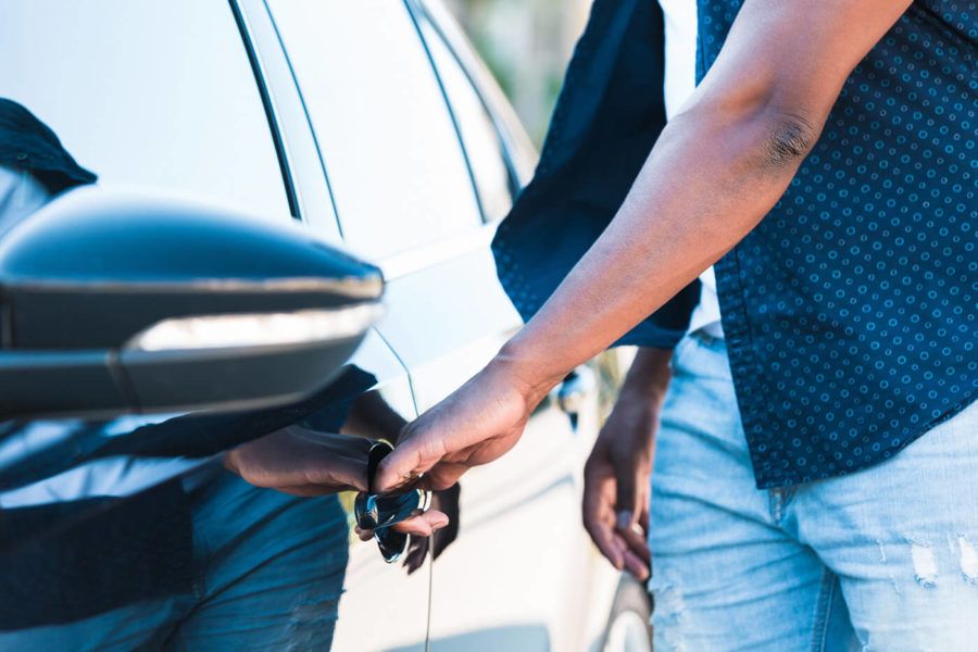 Unrecognizable man reaches for car door handle with left hand 