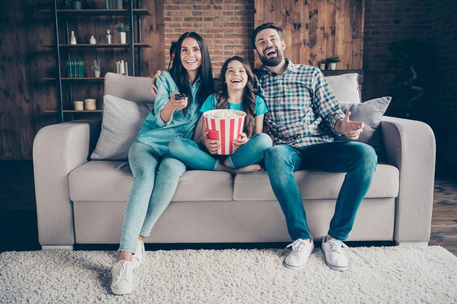 Portrait of cheerful mom dad and little kid have rest laugh look funny film wear denim jeans checkered shirt t-shirt sit divan in house indoors