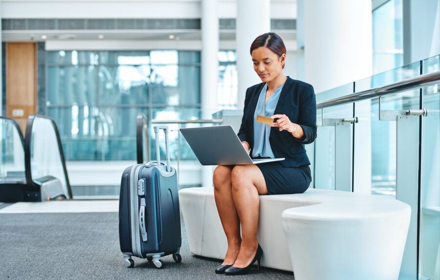 A businesswoman using her laptop and credit card to shop online while sitting in the airport.