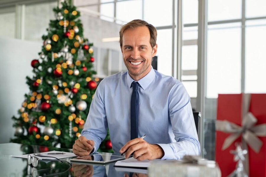 A smiling male bank worker is sitting at his desk with Christmas decorations in the background