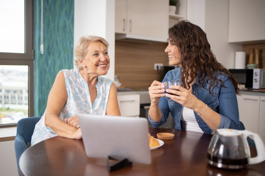Two women sitting together with a laptop at a kitchen table.
