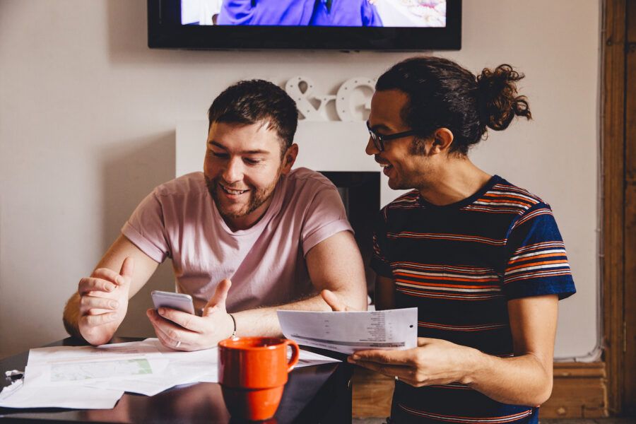 Male couple looking through financial documents together in their home, saving toward a short-term goal.