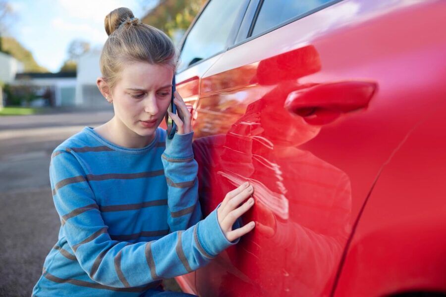 Concerned young woman calling her insurance company while looking at the scratched car door