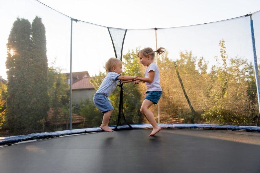 Two young kids jumping on a trampoline on the backyard