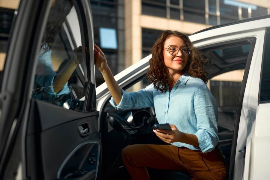 Young business woman getting out of the car while holding her smartphone
