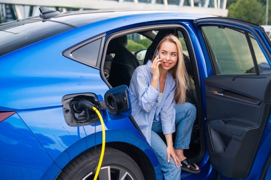 Young woman making a phone call from the back seat while her electric vehicle is plugged in.