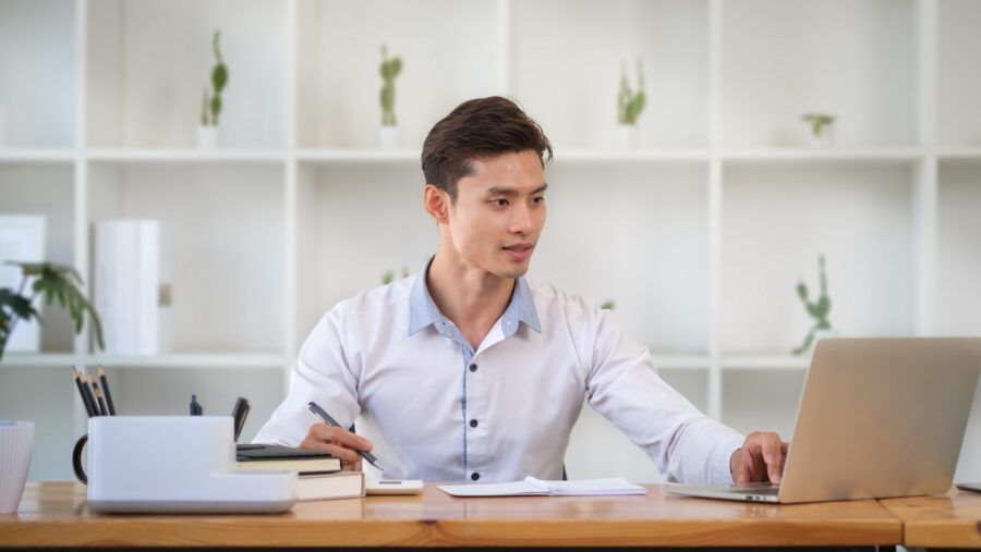 Young man using laptop and doing some paperwork at his personal office.
