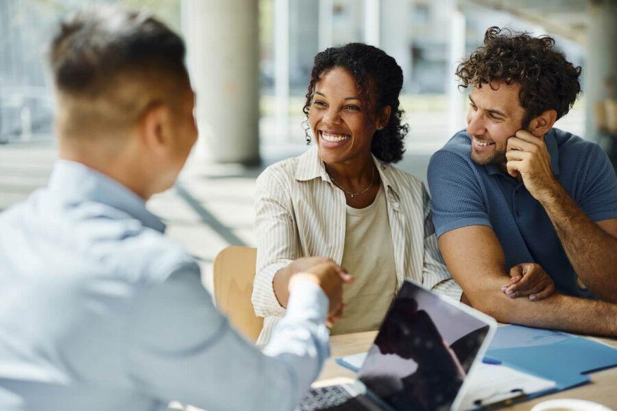 Smiling young woman is shaking hands with a male financial adviser, a happy man seating beside her.