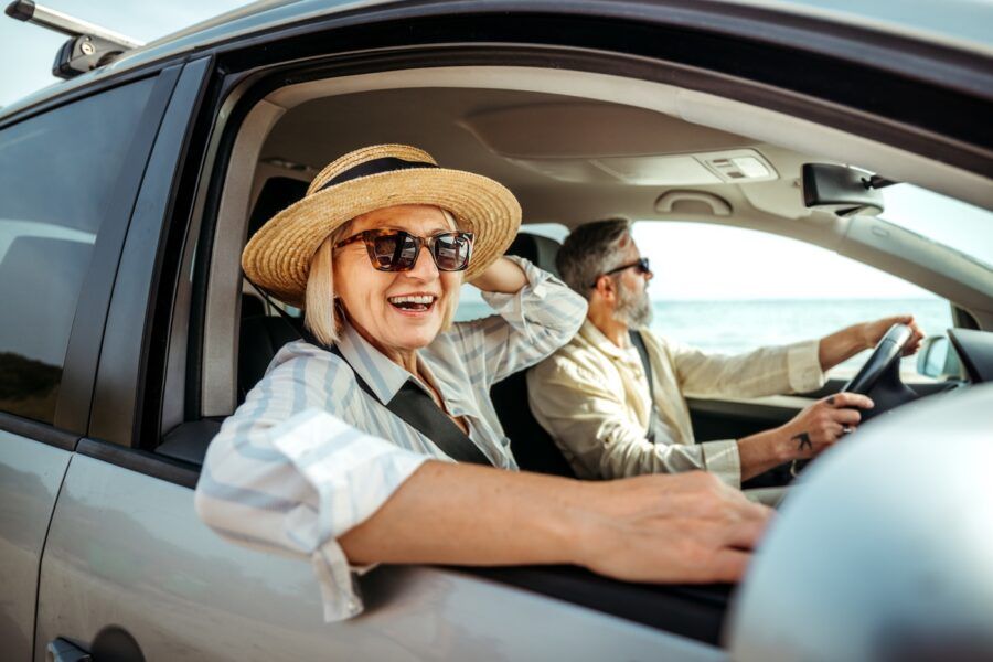 Senior woman leaning through car window while enjoying ride with her husband