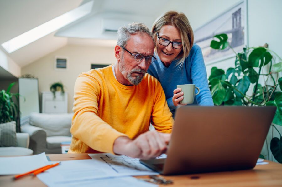 Happy senior couple reviewing finances while using laptop at home.