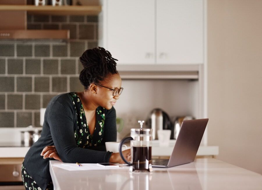 Shot of a young woman researching money market accounts vs money market funds in her kitchen on a laptop.