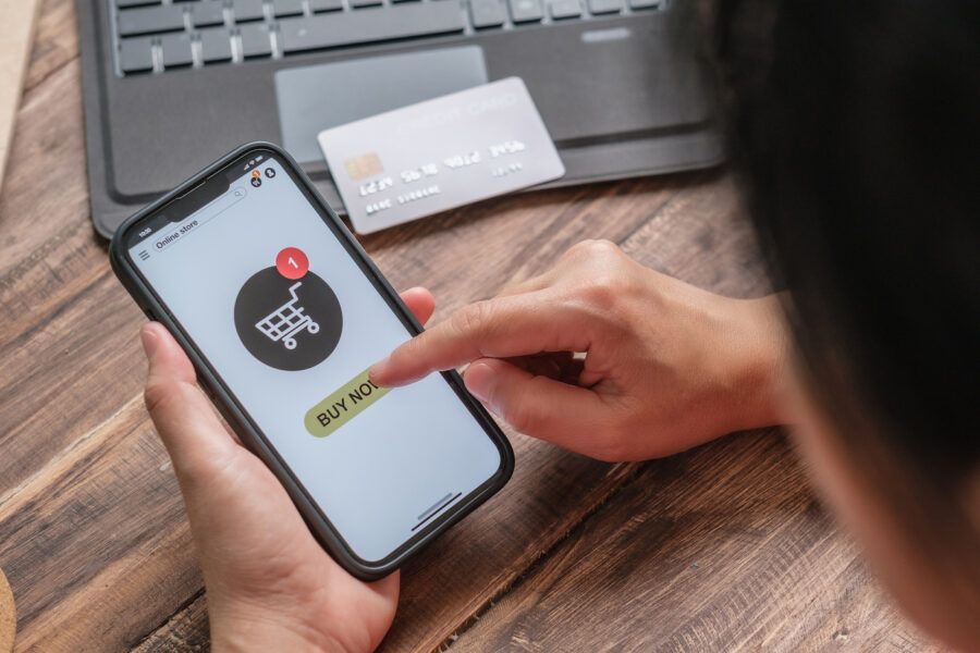 Close-up of a woman's hand shopping online with a mobile app against a wood table at home. She is selecting the