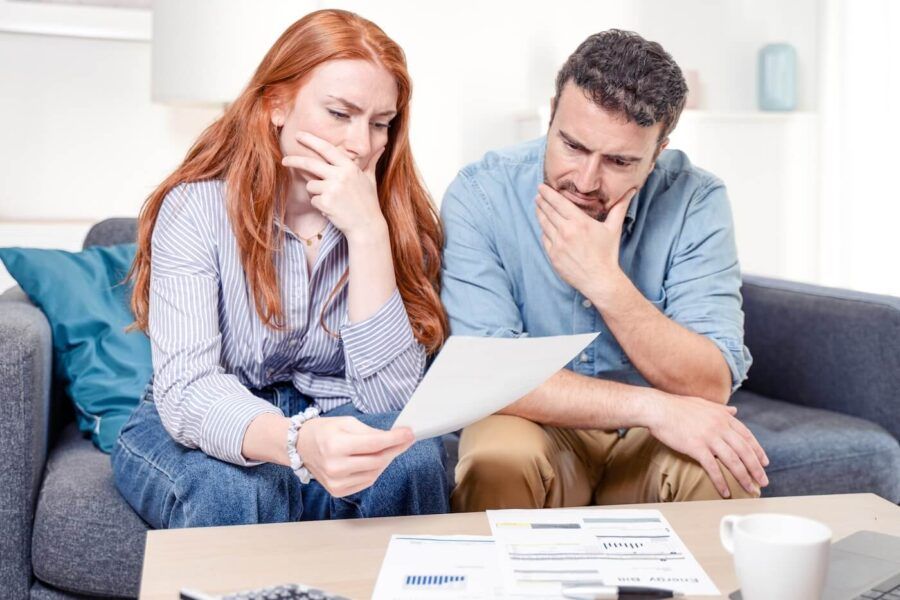 Concerned couple reviewing a document at the coffee table with printed documents and a mug beside them