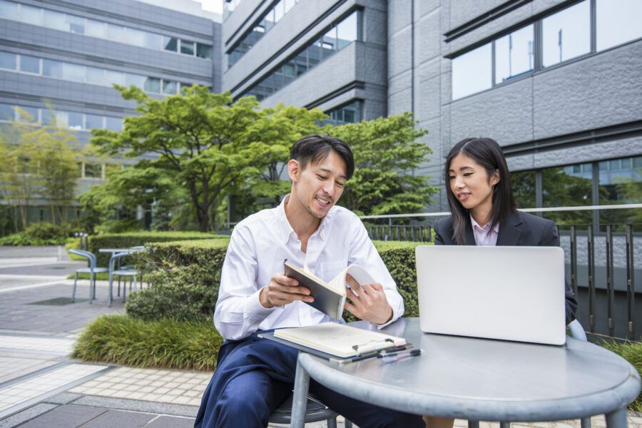 A man meeting with his financial advisor and asking questions. They are sitting outside in a business park at a table with a laptop on it.