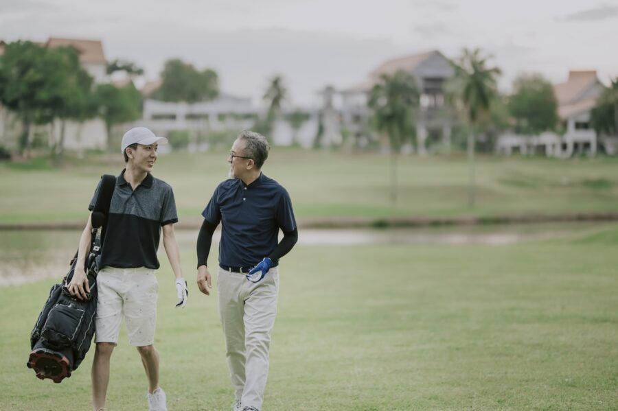 A golfer walking and talking to his son who is carrying golf bag at the end of the game.