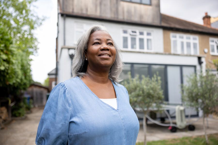 Happy woman smiling outside her house, considering selling before 2 years.