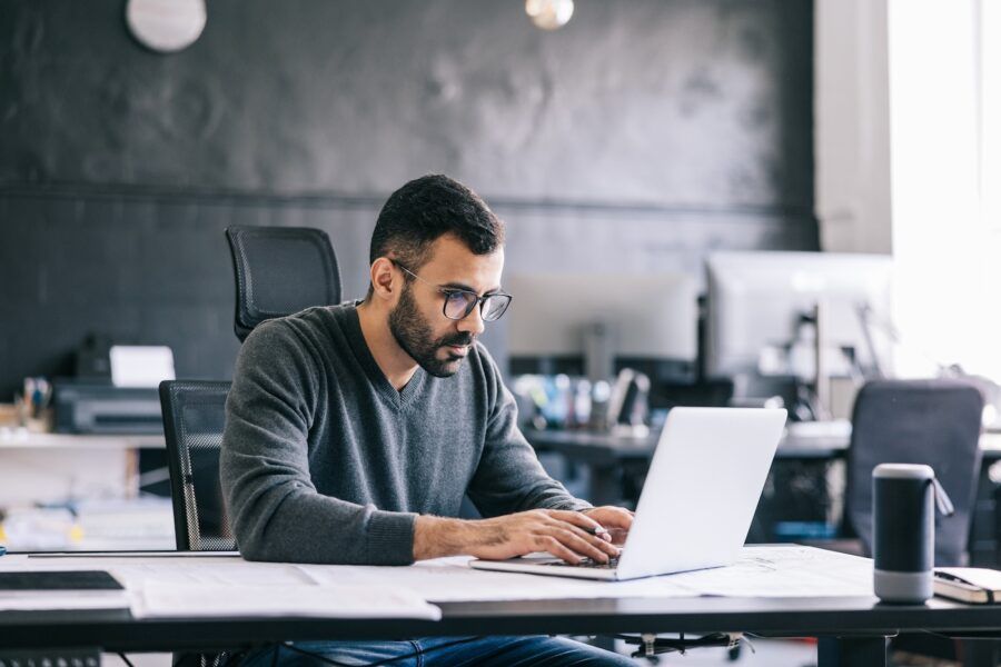 A man sitting in an office looking intently at his savings accounts on his laptop.
