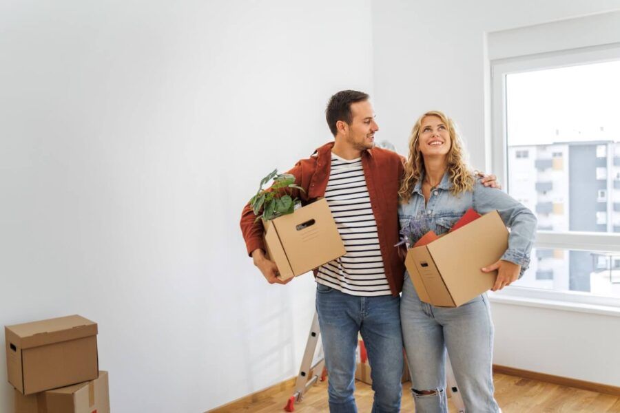 A photo of a young couple standing in their new apartment with the moving boxes