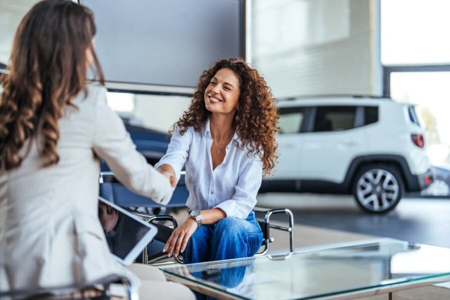 Female agent shaking hands with the smiling female customer in the car dealership