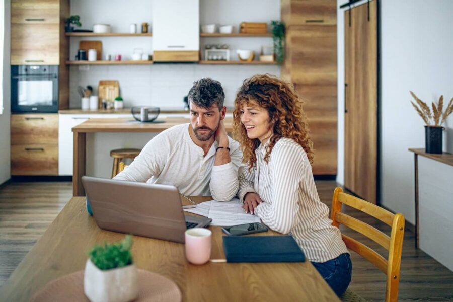 A couple exploring the investment options while sitting in a modern kitchen with a laptop and printed documents beside them