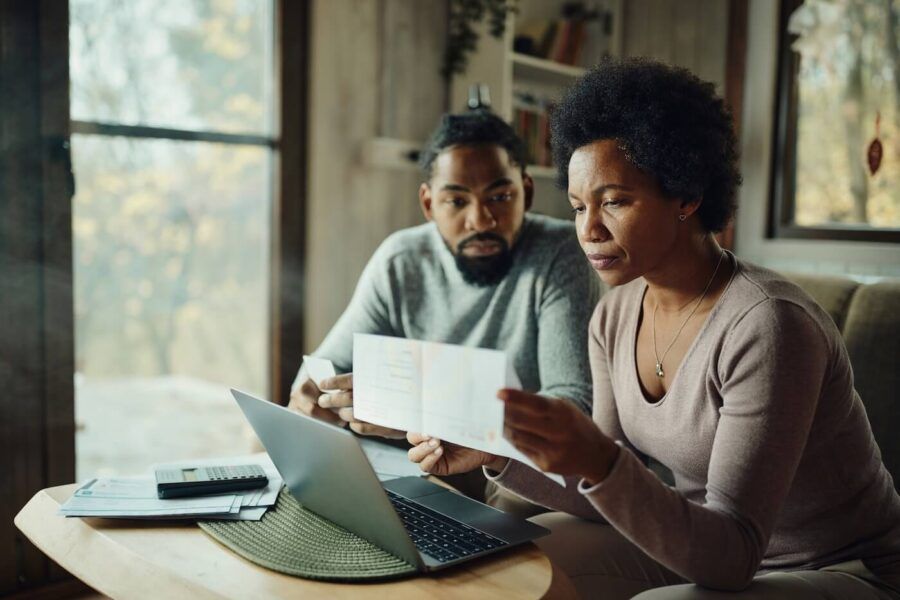 Concerned mature couple reviews paperwork together at a coffee table with a laptop, calculator, and documents beside them