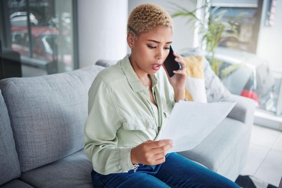 Concerned young woman making a phone call while reviewing printed documents