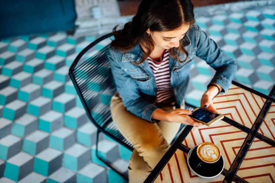 Young woman checking her cryptocurrency wallet on her mobile phone while enjoying cappuccino in the cafe