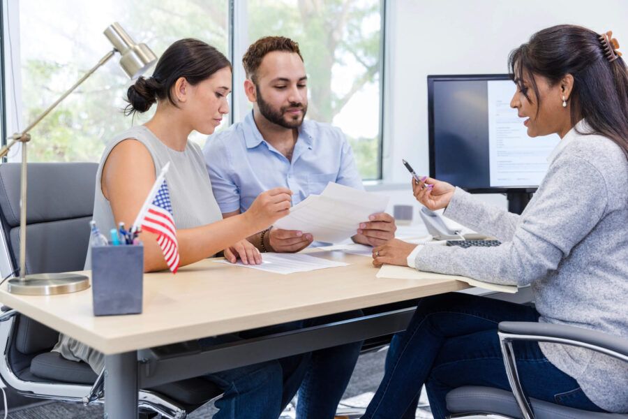 Couple meeting with a female loan consultant in an office, reviewing and discussing loan documents at a desk