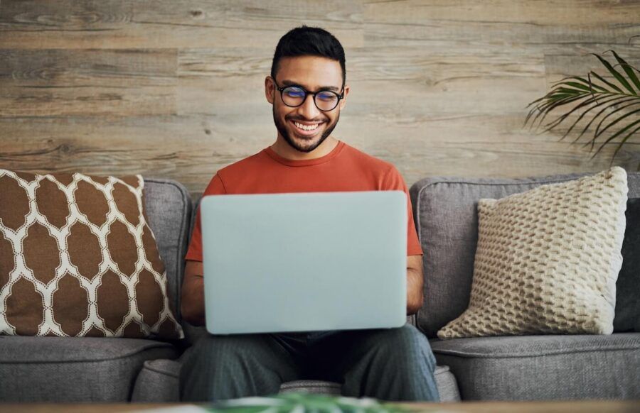 Smiling young man wearing glasses is using his laptop in the living room