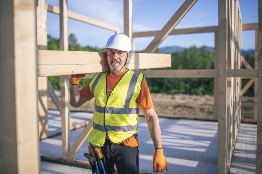 Portrait of a male worker on construction site holding plank beam on his shoulder.