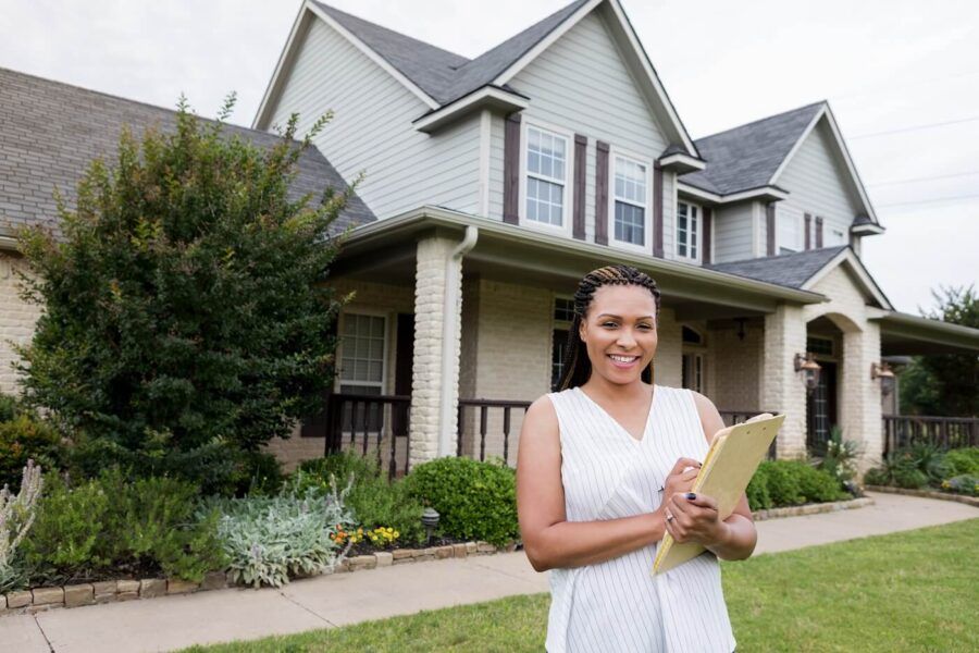 Female home appraiser standing next to a house with a paper pad in her hands