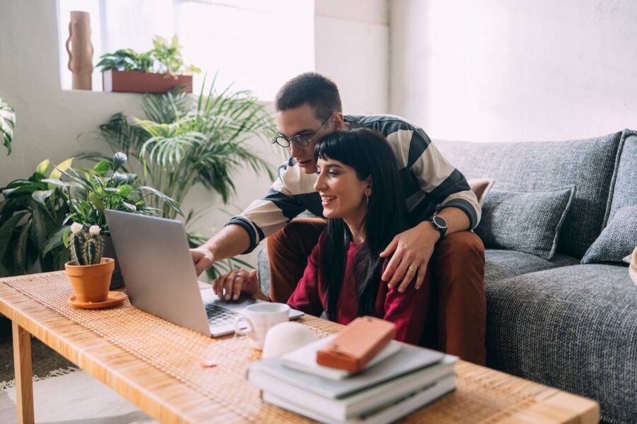 Couple seated in a cozy living room, looking at a laptop screen