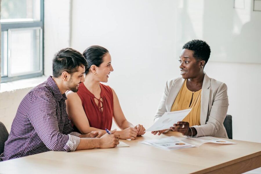 A businesswoman holding papers while explaining the load application fee to a young couple