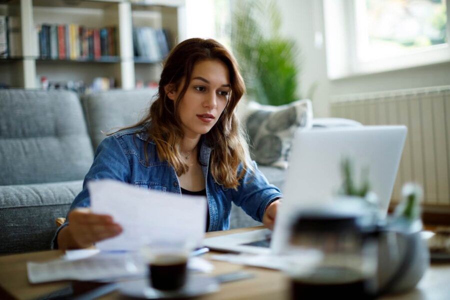 Focused woman using her laptop at home while holding printed documents