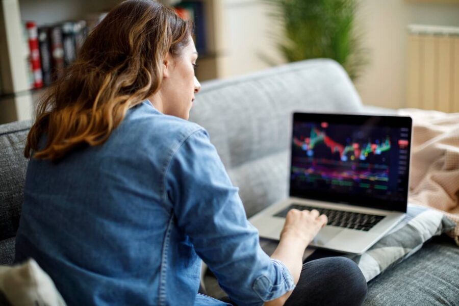 A woman reviewing stock market data on her laptop in a cozy home setting