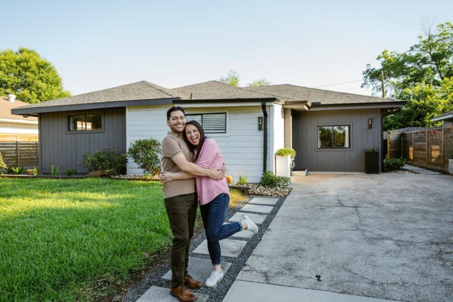 Happy couple hugging each other while standing next to their new house