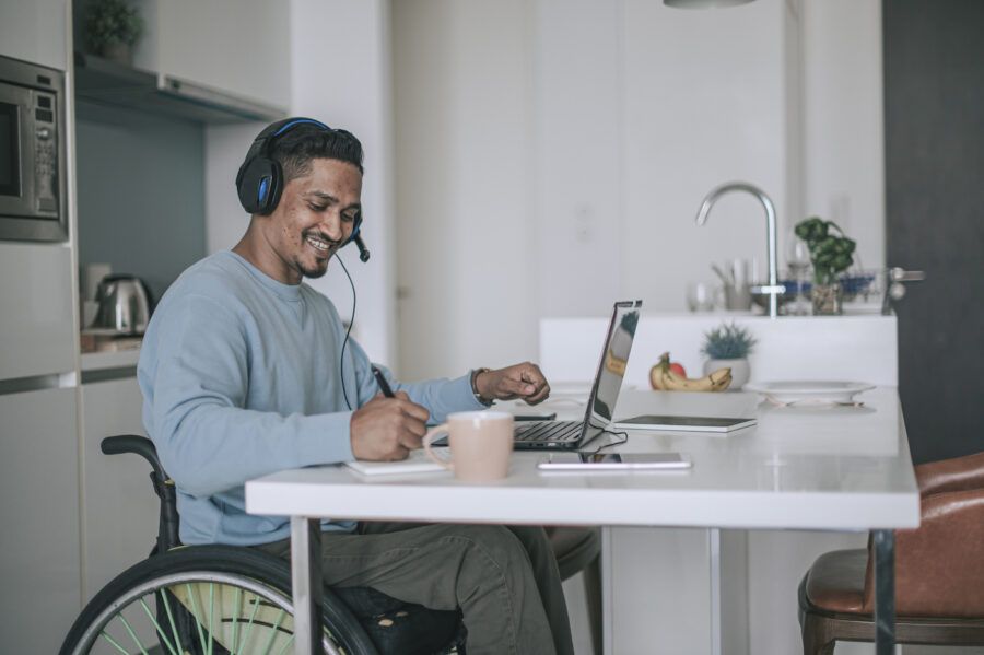A man sitting on a wheelchair in dining room, researching tax advantaged accounts on his laptop.