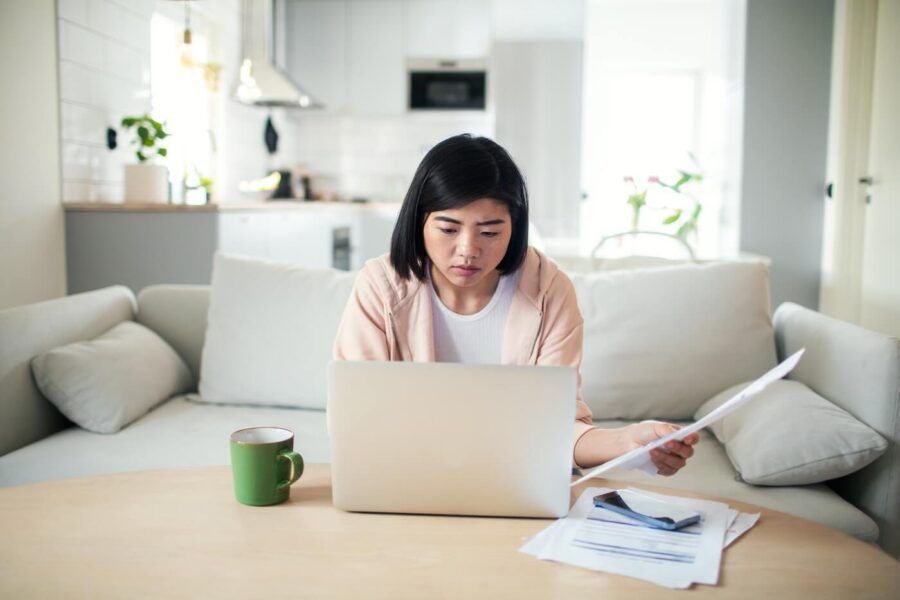 Concerned young woman holding a letter while using her laptop in the living room