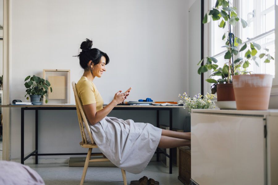 A woman sitting at her desk checking her savings account on her phone